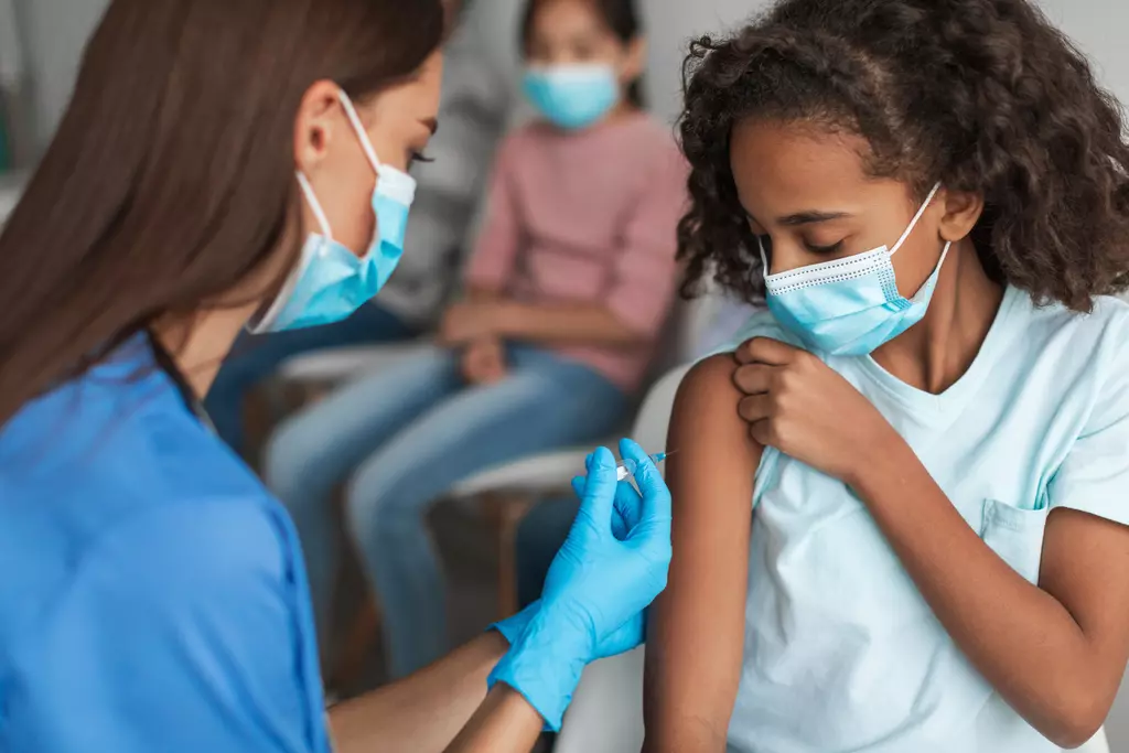 Nurse vaccinating black preteen girl injecting